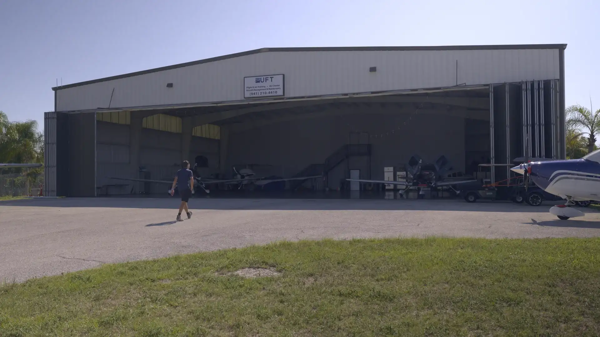 Person walking across the ramp toward the Universal Flight Training hangar at Sarasota Bradenton International Airport
