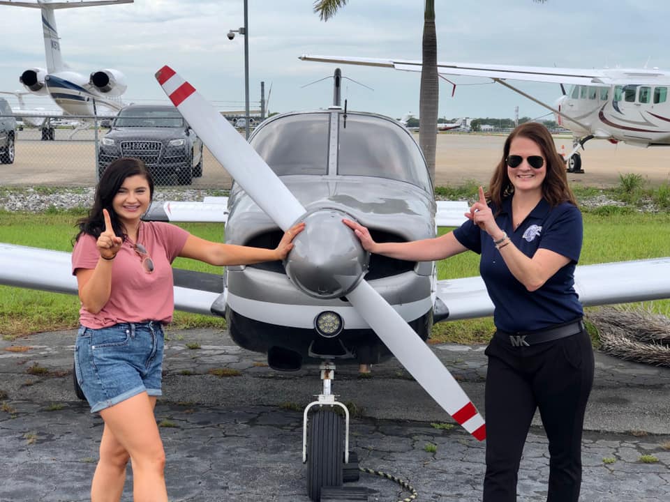Instructor and student pointing up in front of an airplane