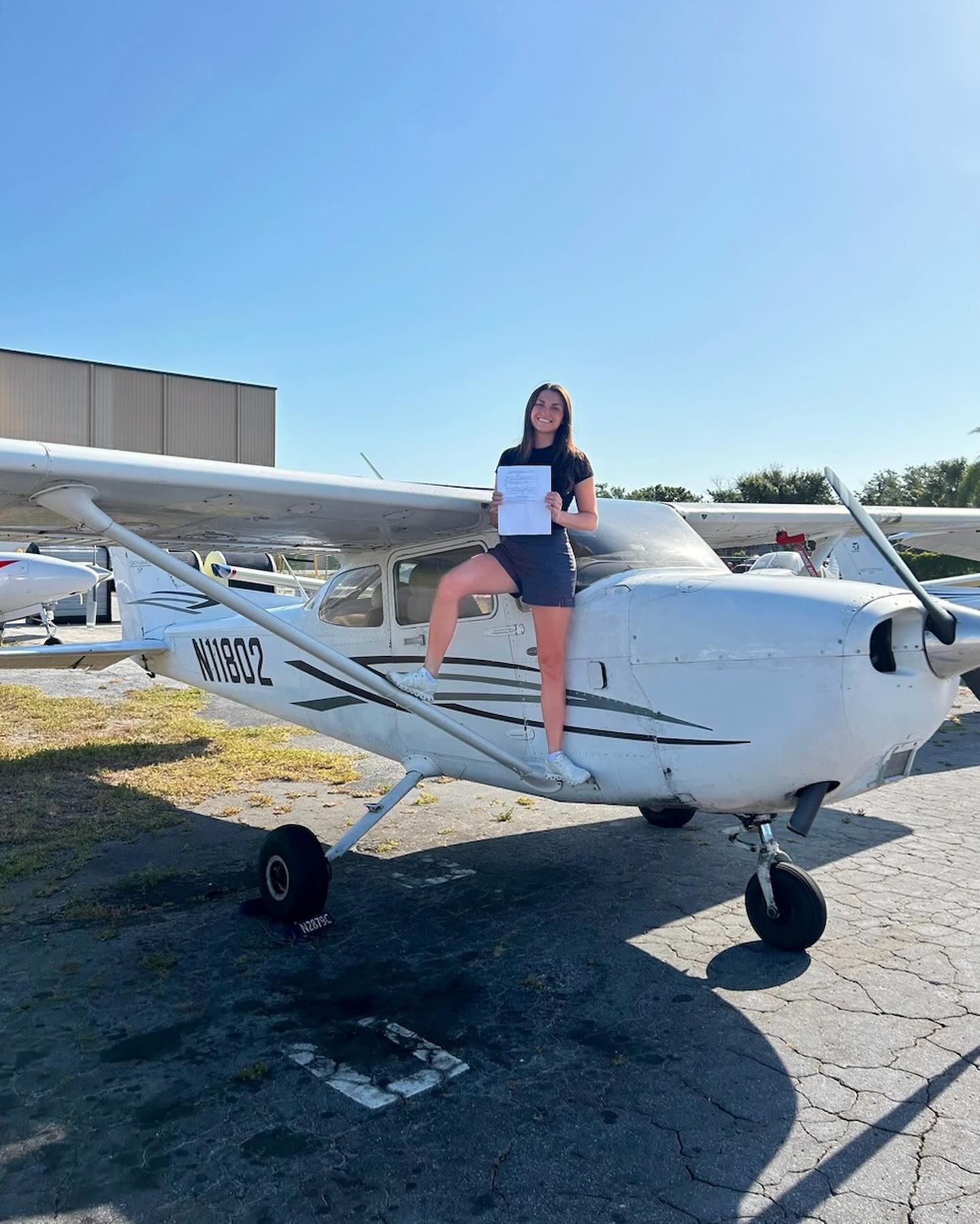 Woman leaning on airplane's wing holding a certificate