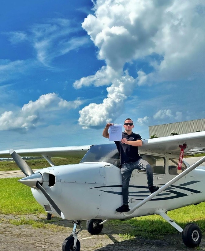 New private pilot sitting on the wing strut of a Cessna 172 holding up a temporary pilot certificate