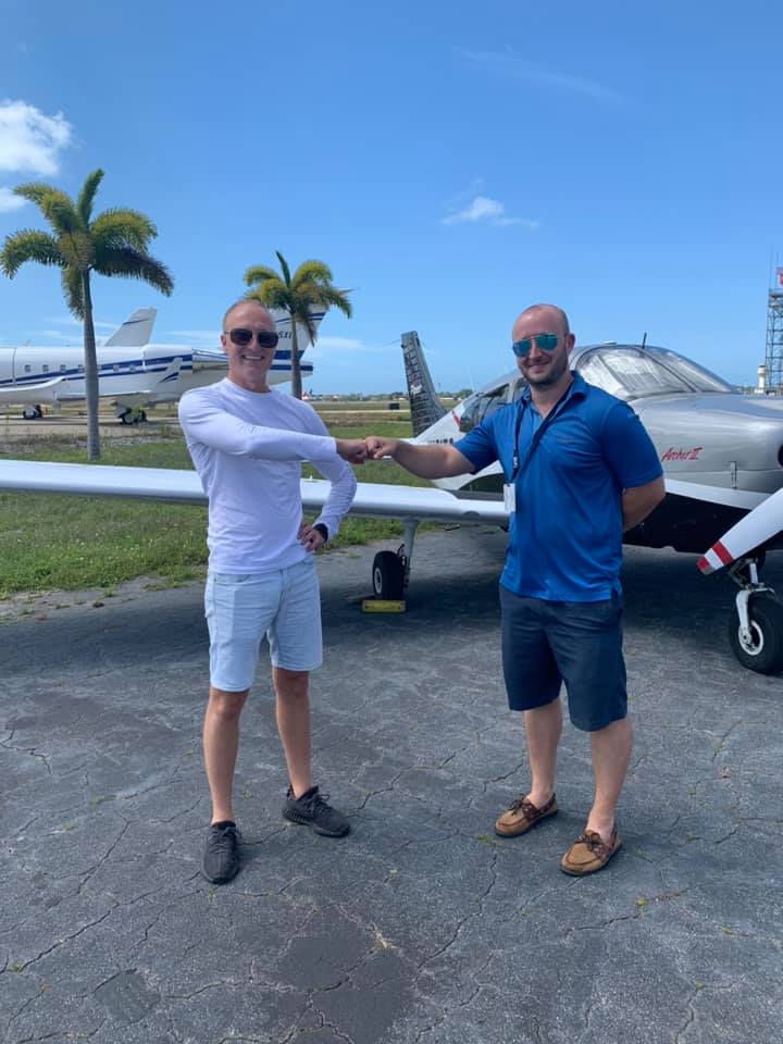 Student and instructor bumping fists in front of an airplane